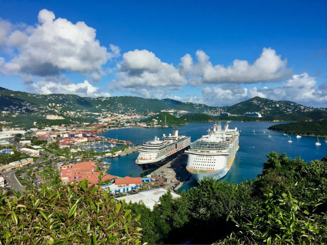 Two cruise ships docked in a Caribbean port harbor surrounded by green hills and blue water for cruise itinerary planning