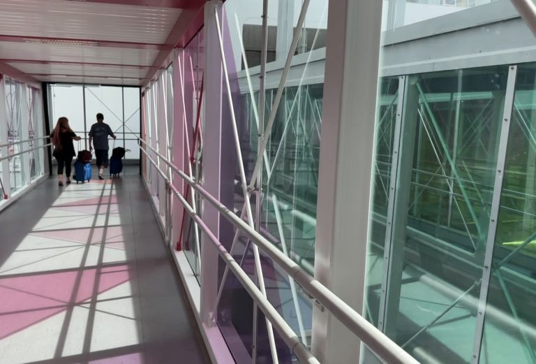 Two travelers with rolling luggage walking through a cruise terminal boarding bridge on cruise embarkation day