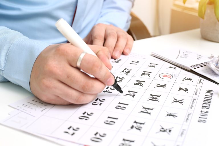 Person in a blue shirt marking dates on an October calendar while planning when to book a cruise